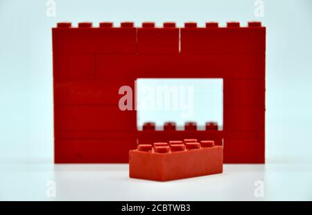 Mur en brique de jouet en plastique rouge avec un bloc manquant et couché devant dans un concept de prise de vue en studio sur l'individualité Banque D'Images