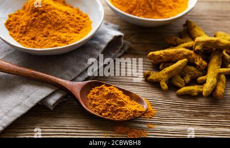 Poudre curcuma jaune et racines sèches sur fond de bois. Banque D'Images