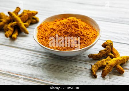 Poudre curcuma jaune et racines sèches sur fond de bois. Banque D'Images