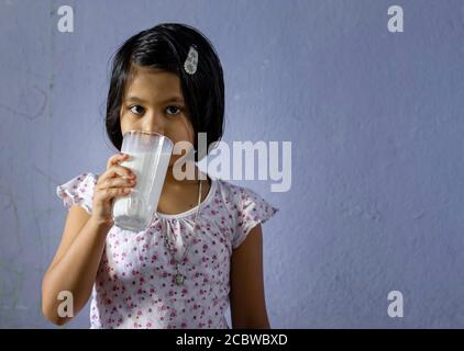 Une petite fille indienne / asiatique mignonne de boire du lait verre et regarder la caméra - concept de saine alimentation Banque D'Images