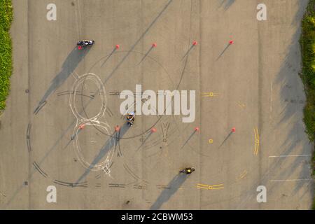 vue aérienne de haut en bas de quatre cavaliers s'amusant sur un parcours avancé de formation de moto slalom entre des cônes orange avec de longues ombres, peintes Banque D'Images