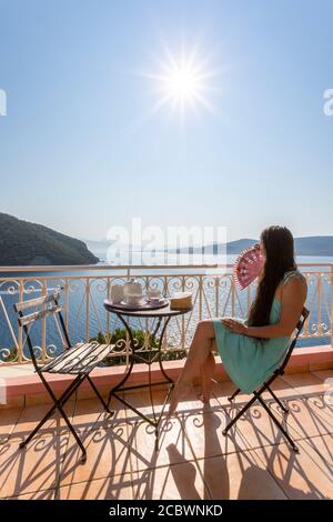 Une fille vêtie sur le balcon d'une villa avec café du matin donne sur une vue sur la côte, Desimi, Lefkada, Iles Ioniennes, Grèce Banque D'Images