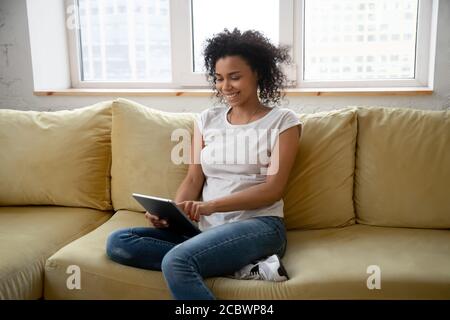 Bonne souriante jeune femme africaine utilisant une tablette à la maison Banque D'Images