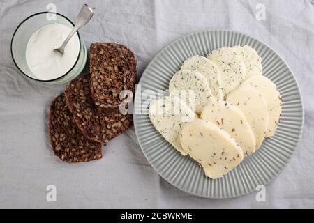 Fromages estoniens au cumin, à l'aneth et à l'ail, tranchés de pain de seigle aux grains, et une tasse de crème aigre Banque D'Images