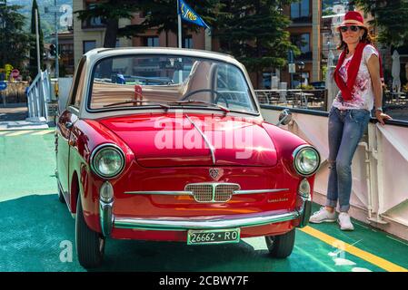 Une femme se trouve à côté d'une voiture classique rouge Autobianchi Bianchina Trasformabile sur le pont d'un ferry sur le lac de Garde, en Italie Banque D'Images