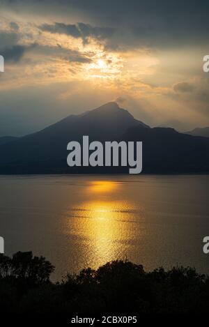 Le soleil du soir brille à travers les nuages orageux au-dessus de Monte Pizzocolo et du lac de Garde, en Italie Banque D'Images