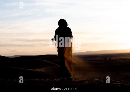 Silhouette de personne sautant et jetant du sable dans le Sahara contre un coucher de soleil Banque D'Images