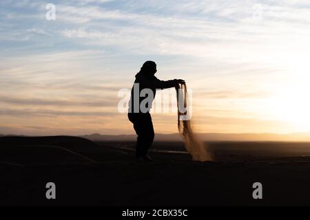 Silhouette de personne sautant et jetant du sable dans le Sahara contre un coucher de soleil Banque D'Images