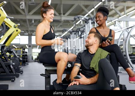 jeunes sportifs parlant en salle de gym, après l'entraînement, les femmes de race mixte et l'homme caucasien se reposant appréciant la conversation terminé l'entraînement Banque D'Images