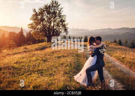 De beaux jeunes mariés se sont envorés dans les montagnes au coucher du soleil. Mariée et marié marchant en été Carpates. Banque D'Images