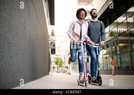 Deux hommes d'affaires souriants conduisant un scooter électrique au travail. Banque D'Images