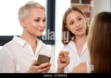 deux stylistes professionnels de maquillage peignent le visage du mannequin. jeune styliste caucasien de beauté préparer une fille attrayante pour la fête, la fête. dans le salon de beauté Banque D'Images