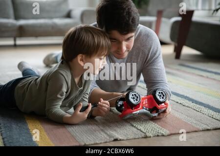 Un jeune père attentionné qui fixe une voiture-jouet avec un fils enfant. Banque D'Images