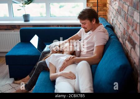 homme beau et prudent avc ventre de femme enceinte, couple marié passer le week-end à la maison, se reposer. homme et femme en tenue domestique, pyjama Banque D'Images