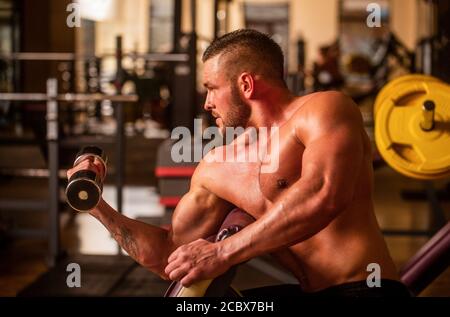 Homme bodybuilder faisant des exercices avec des haltères. Homme de fitness levant l'haltère. Bodybuilder s'entraîner avec des haltères à la salle de gym. Levage d'un homme Banque D'Images