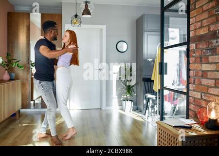 vue latérale sur une belle femme dansant avec un petit ami à la maison. couple interracial en tenue décontractée en mouvement. deux coeurs remplis d'amour. Banque D'Images