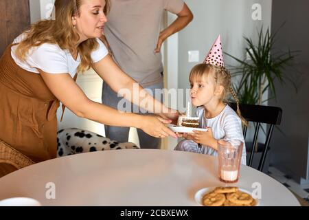 fille sur le point de souffler les bougies sur le gâteau, fête d'anniversaire avec les parents à la maison. concept de fête Banque D'Images