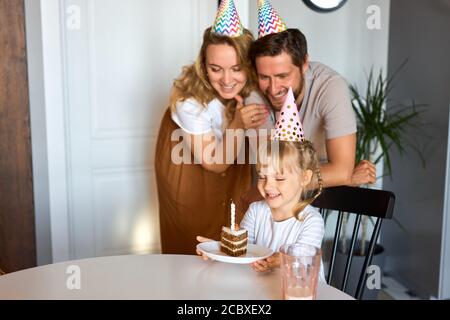 fille sur le point de souffler les bougies sur le gâteau, fête d'anniversaire avec les parents à la maison. concept de fête Banque D'Images