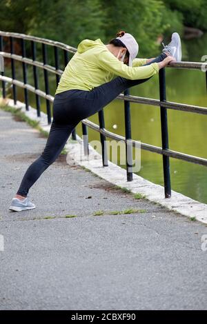 Une femme américaine asiatique agile portant un masque s'étire avant de faire de l'exercice. À Kissena Park, Flushing, New York. Banque D'Images