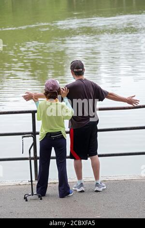 Un aide aide aide un homme ayant des problèmes de santé à faire sa routine d'étirement. Dans un parc à Flushing, Queens, New York. Banque D'Images