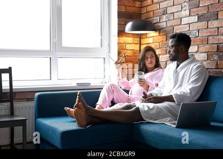 femme enceinte caucasienne avec homme noir. concept de relation de race. ils sont assis sur un canapé à la maison, temps libre le week-end Banque D'Images