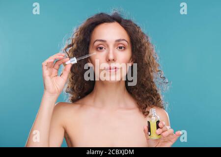 Jeune belle femme avec des cheveux longs ondulés foncés appliquant rajeunissant sérum Banque D'Images