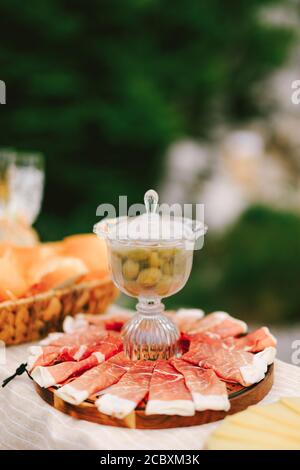Un vase avec de grandes olives vertes sur une assiette ronde pour servir des plats avec du jambon en tranches. Banque D'Images