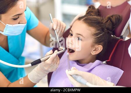 Fille souriante obtenant la guérison de dent de cavité de femme dentiste dans clinique Banque D'Images