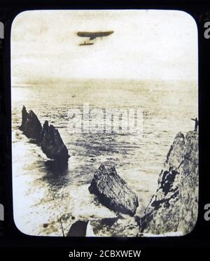 Une diapositive magique représentant l'aviateur français Léon Morane dans son monoplan Bleriot pendant son vol vers le phare Needles, à une distance de 21 miles en 25 minutes. Ce fut fait le 17 juillet 1910 lors de son apparition au Bournemouth Air Show. Diapositive publiée par W. Butcher & Sons, Londres et datant d'environ 1914. Banque D'Images