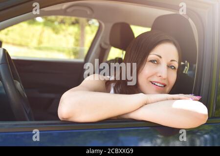 Femme souriante pilote regardant la voiture. Portrait d'une femme souriante assise dans la voiture, regardant l'appareil photo. Banque D'Images