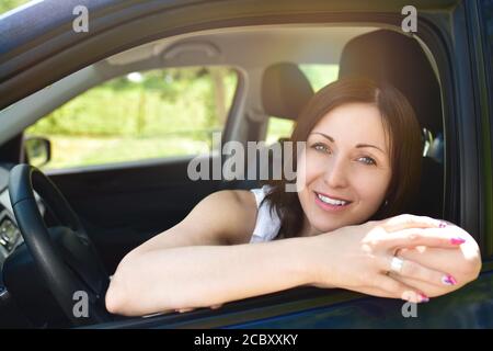 Femme souriante pilote regardant la voiture. Portrait d'une femme souriante assise dans la voiture, regardant l'appareil photo. Banque D'Images