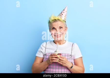 drôle de granny a cuit le gâteau de tasse pour son petit-fils, vieille femme fraîche dans les vêtements de mode se préparant pour une fête. femme mature se souvient de son enfance Banque D'Images