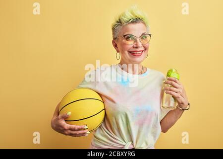 positive drôle femme avec les cheveux jaunes est l'affection du jeu de bakettball, portrait de gros plan, isolé fond jaune. Banque D'Images