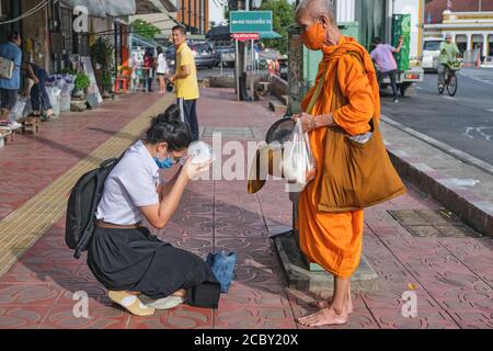 Au cours de sa matinée, un moine bouddhiste bénit une étudiante à genoux, qui tient une offrande dans sa main; Bangkok, Thaïlande Banque D'Images