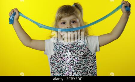 Enfant qui s'amuse à faire de la chaux turquoise. Enfant jouant avec un jouet fait à la main. Drôle d'élève fille. Détente et satisfaction. Solimette verte curieusement satisfaisante pour un plaisir absolu et un soulagement du stress. Arrière-plan jaune Banque D'Images