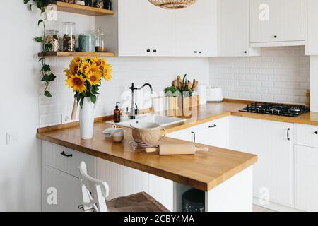 Plats et ustensiles sur table de cuisine, prêts à cuisiner. Cuisine blanche simple et moderne de style scandinave, détails de la cuisine, table en bois, bouq tournesol Banque D'Images
