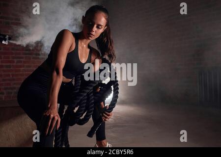 Une femme se repose après son entraînement en salle de sport. Faites de l'exercice avec des cordes dans la salle de sport. Arrière-plan Brickwall Banque D'Images