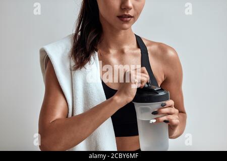 Femme imreconnaissable avec bouteille en plastique d'eau dans les mains, de beaux doigts, des ongles. Corps sportif. Fitness, sport concept. Isolé dans le dos gris Banque D'Images