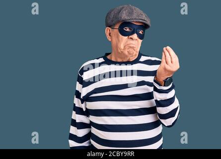 Homme de haut niveau portant un masque de cambriolage et un t-shirt faisant de l'italien geste avec la main et les doigts expression sûre Banque D'Images