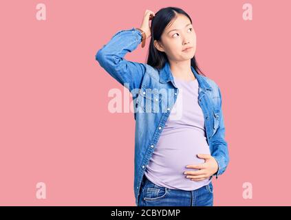 Jeune femme chinoise enceinte s'attendant à un bébé, se méprendre et se demander des questions. Incertain avec doute, pensant à la main sur la tête. Pensive Banque D'Images