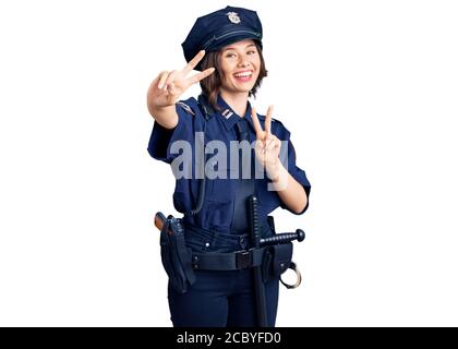 Jeune belle fille portant l'uniforme de police souriant regardant la caméra montrant les doigts faisant signe de victoire. Numéro deux. Banque D'Images