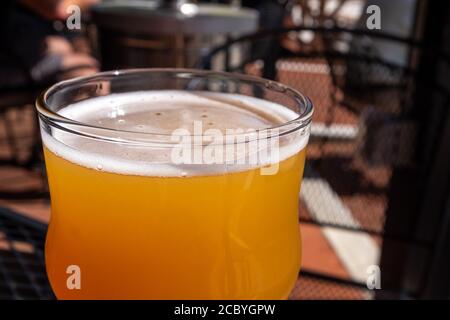 Gros plan d'une bière aigre dans un verre à bière transparent.Le liquide est assis au bord d'une table en métal sur un patio d'une microbrasserie. Banque D'Images