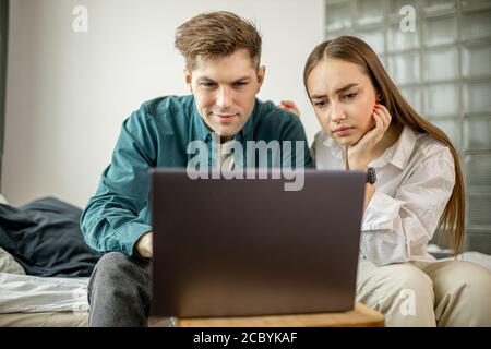 un jeune couple caucasien regarde un film sur ordinateur portable à la maison, homme et femme en tenue domestique passent du temps libre ensemble. à l'intérieur Banque D'Images