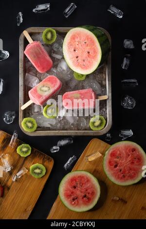 La crème glacée au kiwi et au melon d'eau maison ou aux pop-sicles sont garrées fruits et morceaux de glace sur table noire Banque D'Images