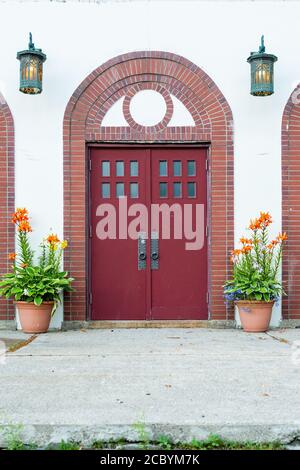 Deux grandes portes rouges avec de petites fenêtres carrées sur le dessus des portes en bois et une fenêtre courbe en demi-cercle sur l'entrée flanquée de pots de fleurs. Banque D'Images