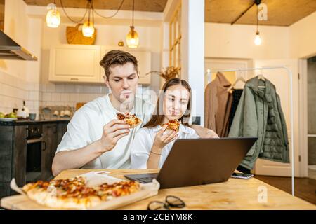 un jeune couple marié caucasien goûte une pizza italienne à la maison, ils ont commandé la livraison à domicile, profiter de temps libre ensemble, regarder le film Banque D'Images