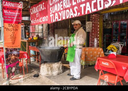 Le cuisinier d'un petit restaurant de bord de route à San Bartolo Coyetepec rade le porc pour les carnitas tacos sur un feu de bois près d'Oaxaca, au Mexique. Banque D'Images