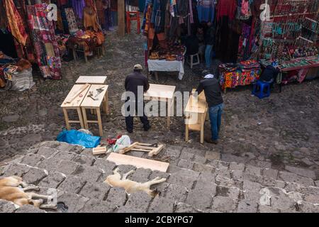 Deux hommes construisent des meubles dans le marché extérieur en face de la chapelle du Calvaire à Chichicatenango, au Guatemala, tandis que les chiens dorment sur les marches de l'église. Banque D'Images