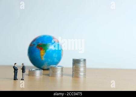 Miniature People Business concept - Partenariat commercial mondial, avec homme d'affaires, pile de pièces et globe Banque D'Images