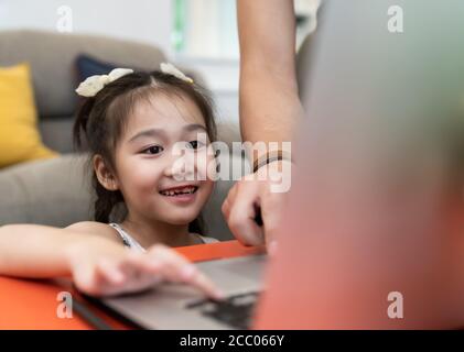 Jeune fille asiatique étudiant élémentaire utilisant un ordinateur portable pour l'apprentissage en ligne et l'étude à partir de l'école tandis que la ville verrouillée de la pandémie COVID-19. Maison schooli Banque D'Images